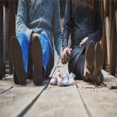 A couple holding hands with baby shoes in front of them