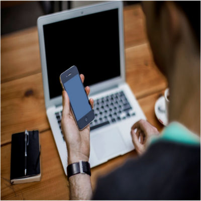 A person looking at a phone in front of a computer